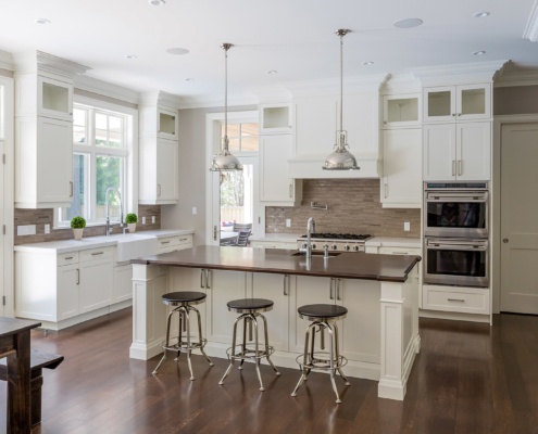 White kitchen with large island, tile backsplash and dark wood floors.