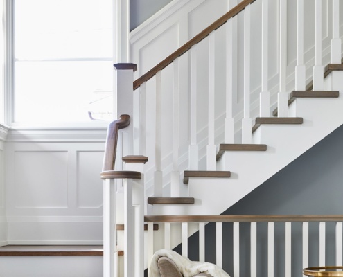 White staircase with wood treads, white wainscoting and white frame window.