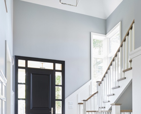 Front entry with black front door, wood floor and white wainscoting.