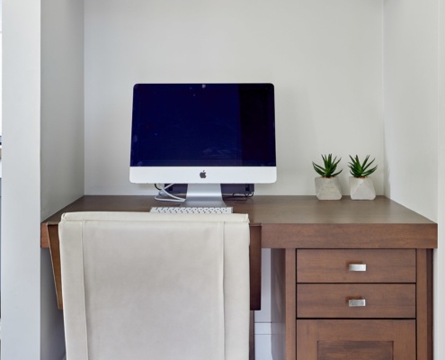 Home office with built in desk, gray wall and wood shelf.
