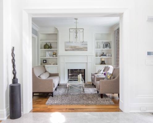 Sophisticated living room with white fireplace, white shelves and hardwood floors.