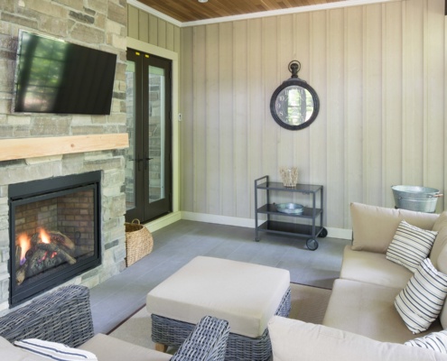 Outdoor deck with tile floor, stone fireplace and wood siding.