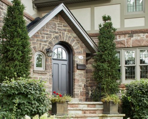 Traditional home front entry with black front door, stone steps and arched window.