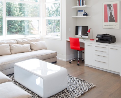 Den with white windows, floating shelves and hardwood floor.