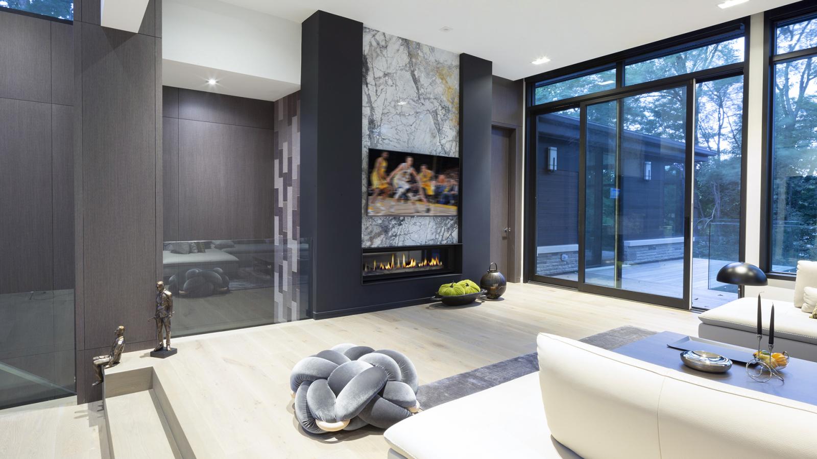 Living room with marble fireplace, wood wall and black frame windows.