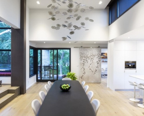 Dining room with modern chandelier, white chairs and light wood floor.