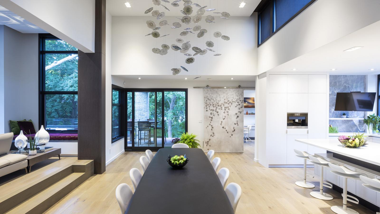 Dining room with modern chandelier, white chairs and light wood floor.