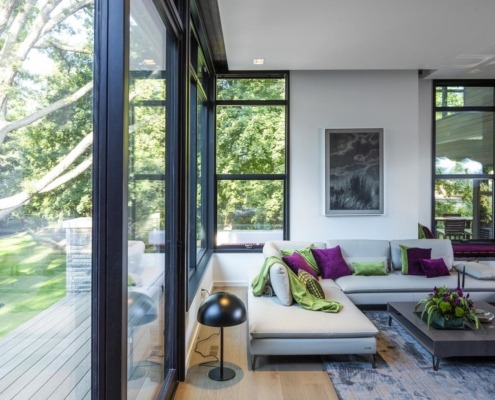 Family room with hardwood floor, floor to ceiling windows and beige couch.