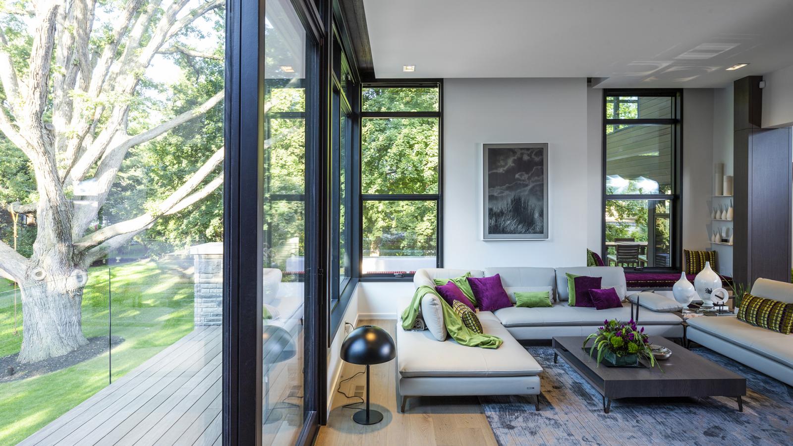 Family room with hardwood floor, floor to ceiling windows and beige couch.