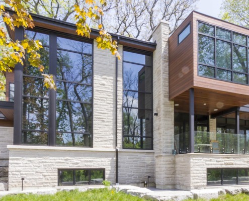 Contemporary home with flat roof, stone siding and glass railing.