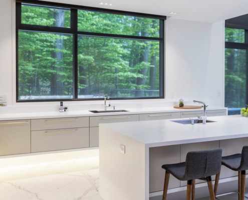 Modern kitchen with gray drawers, black frame windows and white island.