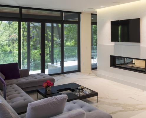 Living room with white fireplace, floor to ceiling windows and gray couch.