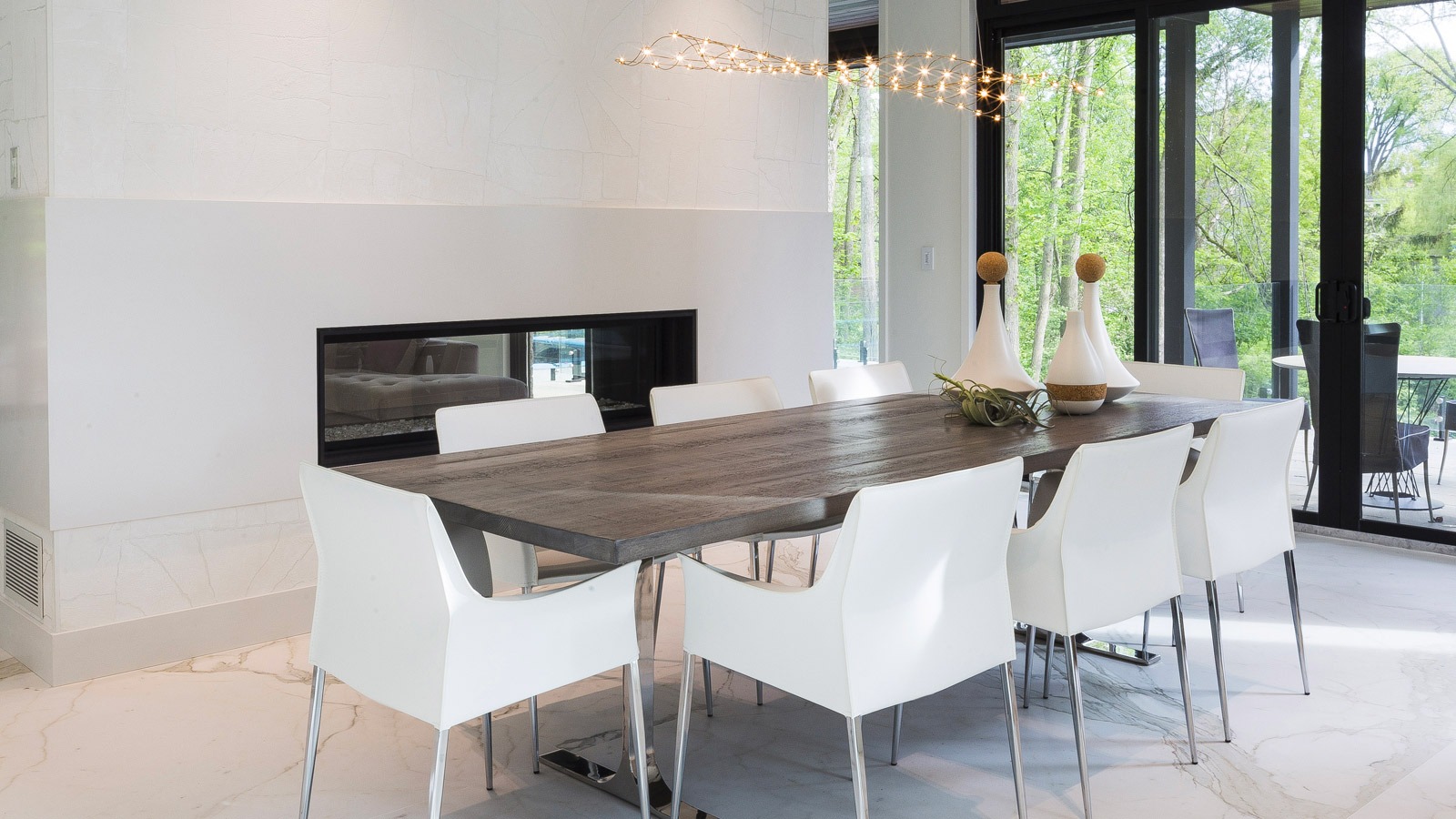 Dining room with double sided fireplace, white chairs and wood table.