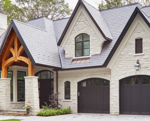 Stone house with metal roof, black frame windows and wood portico.