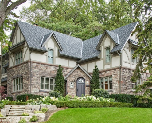 Tudor style home with stone skirt, beige trim and shingled roof.