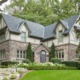 Tudor style home with stone skirt, beige trim and shingled roof.