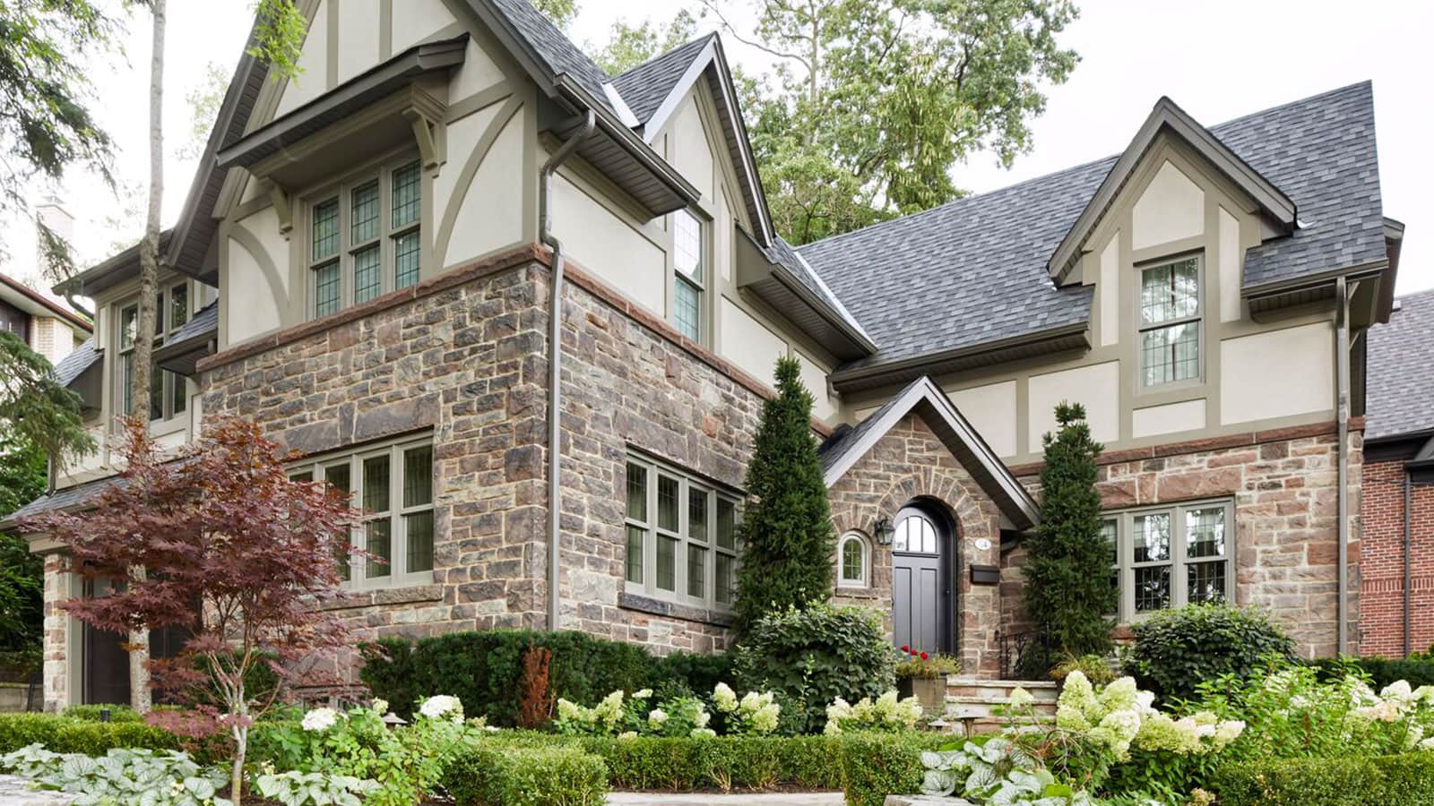Stone house with gables, shingled roof and dark front door.