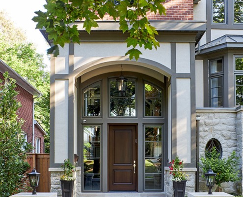 Home front entry with wood front door, oval window and stucco siding.