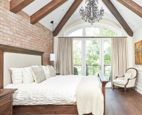 Master bedroom with wood bed, exposed brick and white wainscoting.
