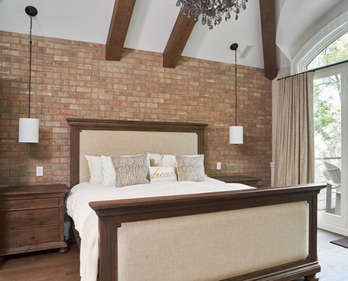 Bedroom with exposed brick, wood beam and white frame window.