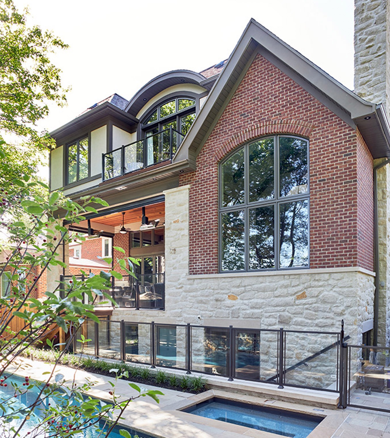 Red brick house with stone siding, glass railing and stucco.