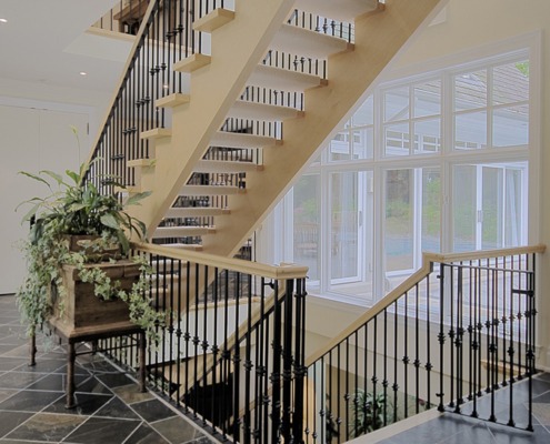 House hallway with wood staircase, white frame windows and tile floor.