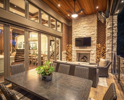 Covered deck with brick wall, floor to ceiling window and stone fireplace.