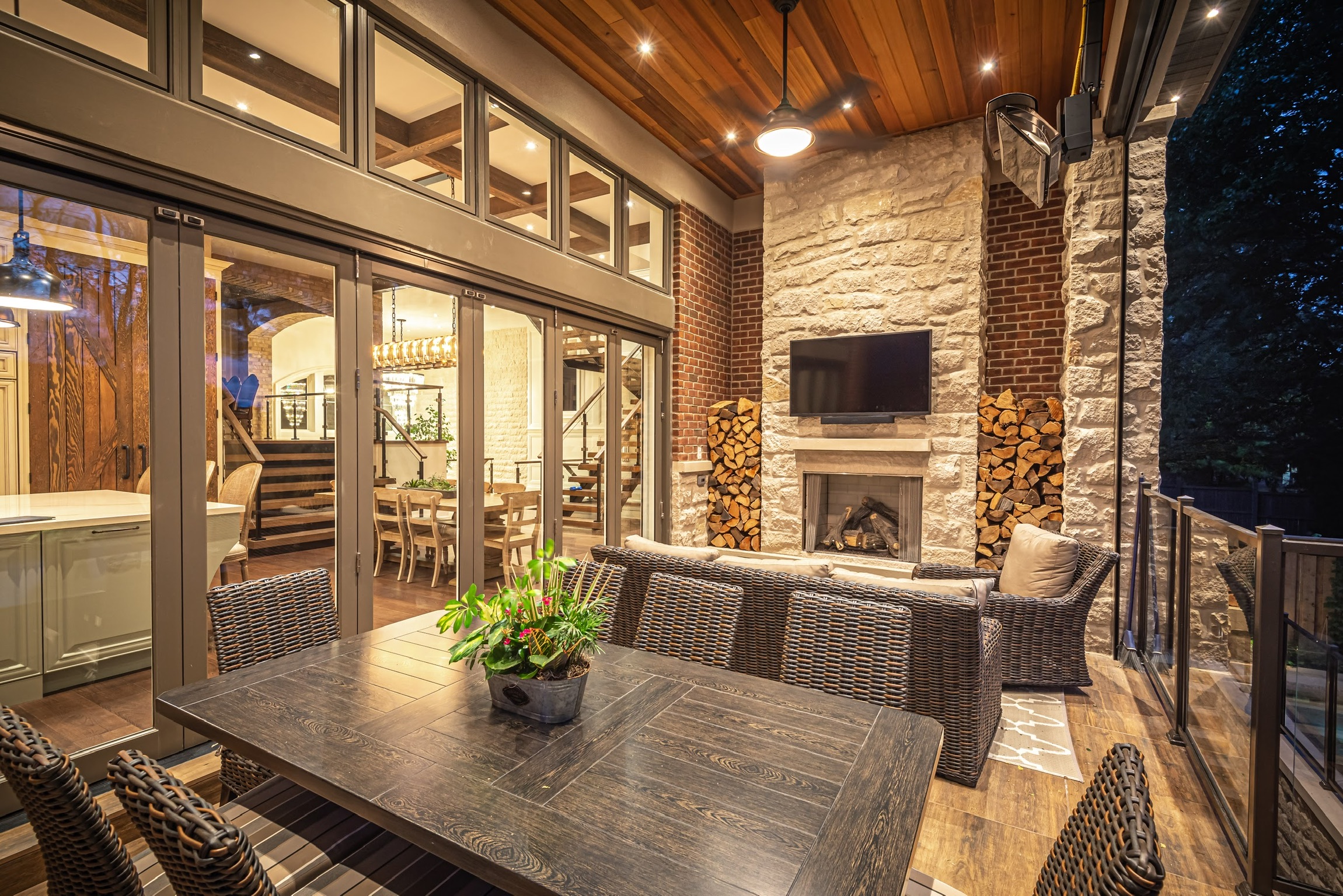 Covered deck with brick wall, floor to ceiling window and stone fireplace.