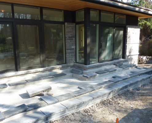 Building flag stone deck for contemporary house with black frame windows.