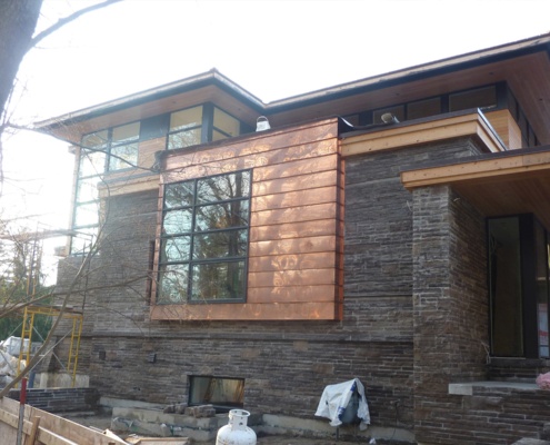 Construction site for modern house with copper siding and stone.