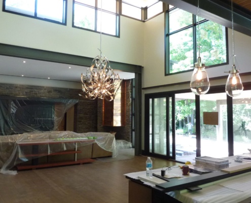 Construction of dining room with modern chandelier, black frame windows and high ceilings.