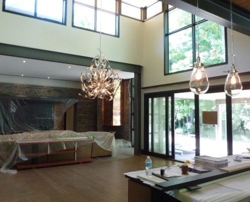 Construction of dining room with modern chandelier, black frame windows and high ceilings.